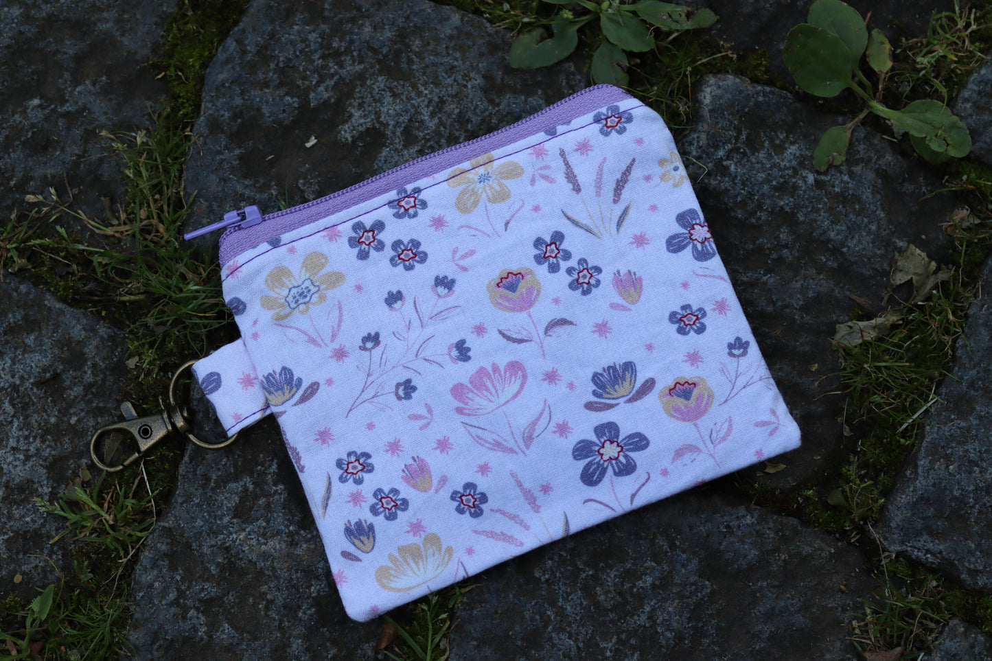 Handgenähtes Täschchen mit lila Blumenmuster und Karabiner – kompakt und stilvoll für unterwegs.