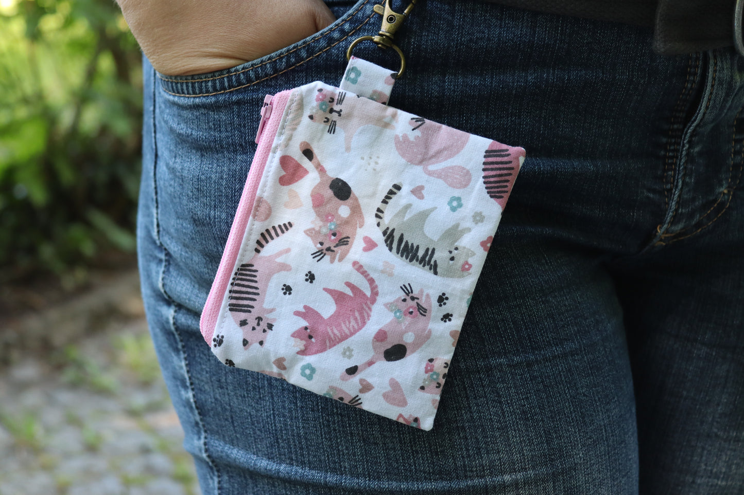 Tragebeispiel Handgenähtes Täschchen (12,5 × 10 cm) mit rosa Katzenmotiven, antikfarbenem Karabiner und rosa Reißverschluss – ideal für Kleinigkeiten unterwegs.