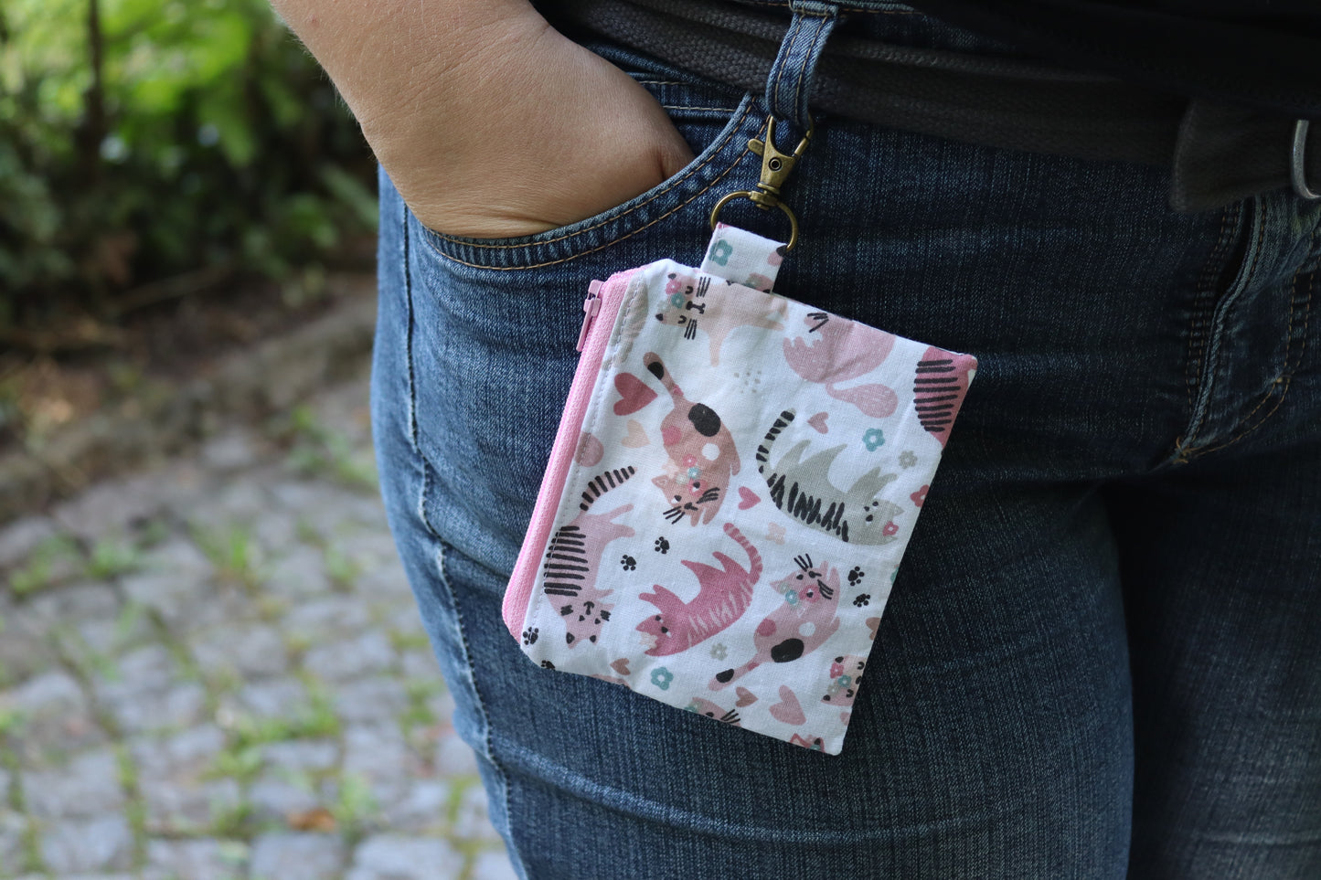 Tragebeispiel Handgenähtes Täschchen (12,5 × 10 cm) mit rosa Katzenmotiven, antikfarbenem Karabiner und rosa Reißverschluss – ideal für Kleinigkeiten unterwegs.
