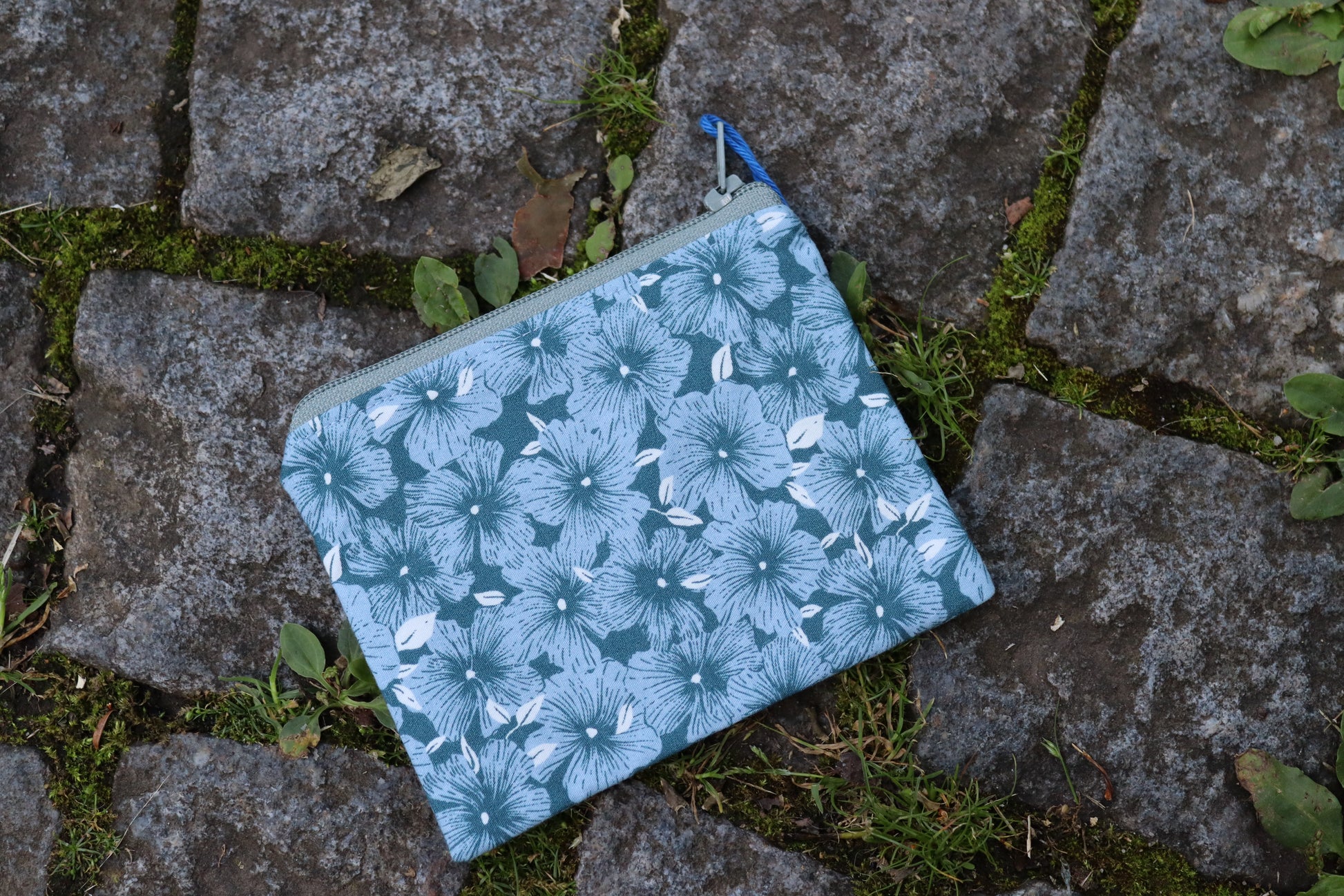 Handgenähtes Täschchen aus blauem Stoff mit hellblauen Blumenmotiven und oliv-farbenen Reißverschluss – ideal für Karten, Kleingeld oder kleine Utensilien.​