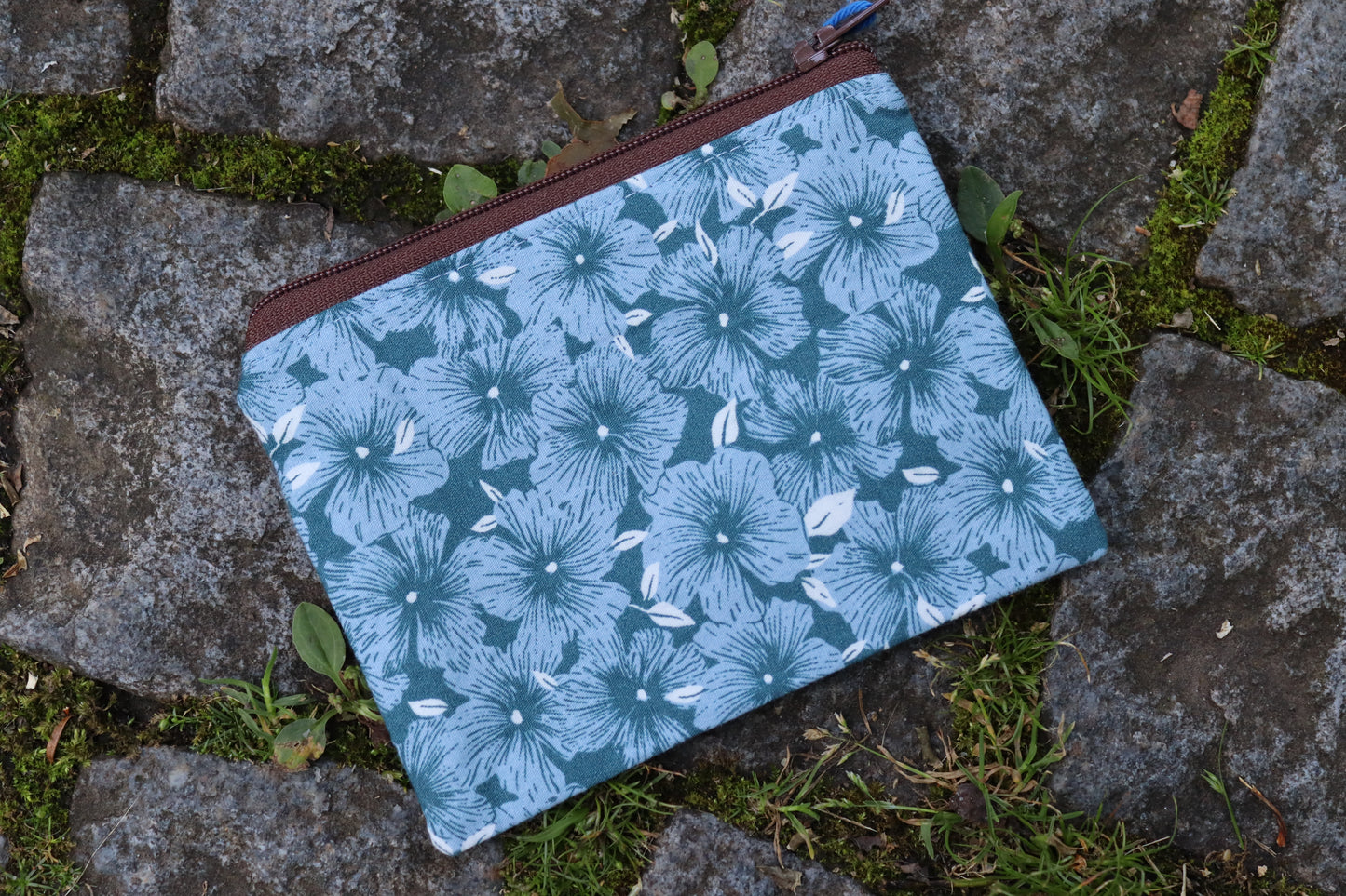 Handgenähtes Täschchen aus blauem Stoff mit hellblauen Blumenmotiven und braunem Reißverschluss – ideal für Karten, Kleingeld oder kleine Utensilien.​