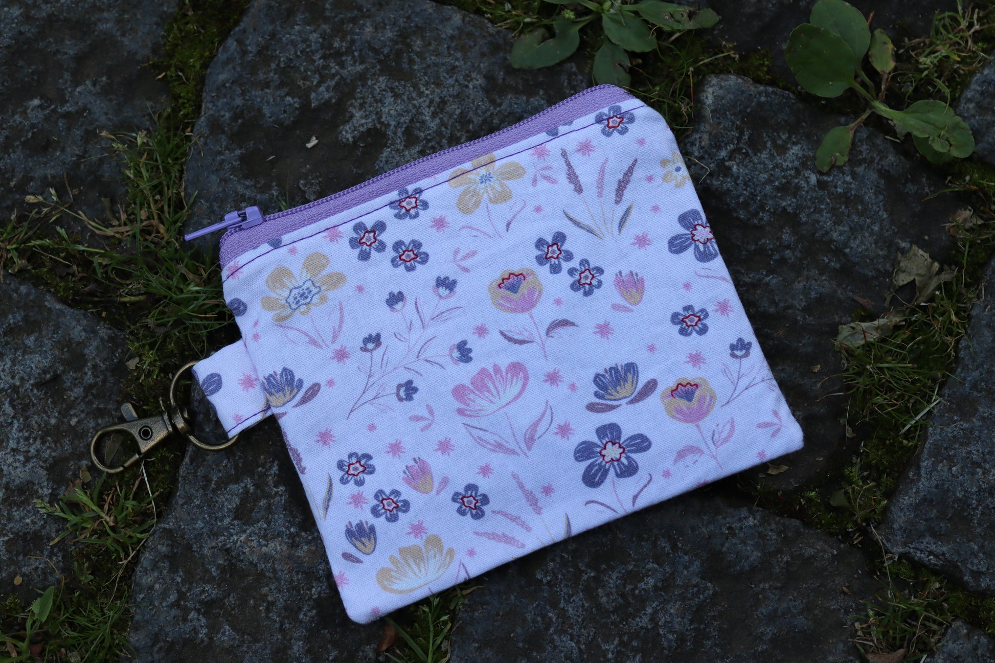 Handgenähtes Täschchen mit lila Blumenmuster und Karabiner – kompakt und stilvoll für unterwegs.