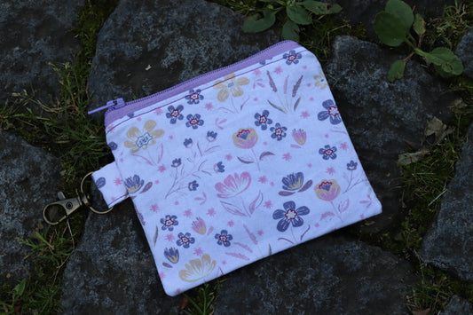 Handgenähtes Täschchen mit lila Blumenmuster und Karabiner – kompakt und stilvoll für unterwegs.